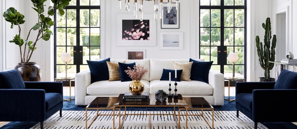 Modern glam living room with white sofa, navy chairs, black-framed windows, and brass accents