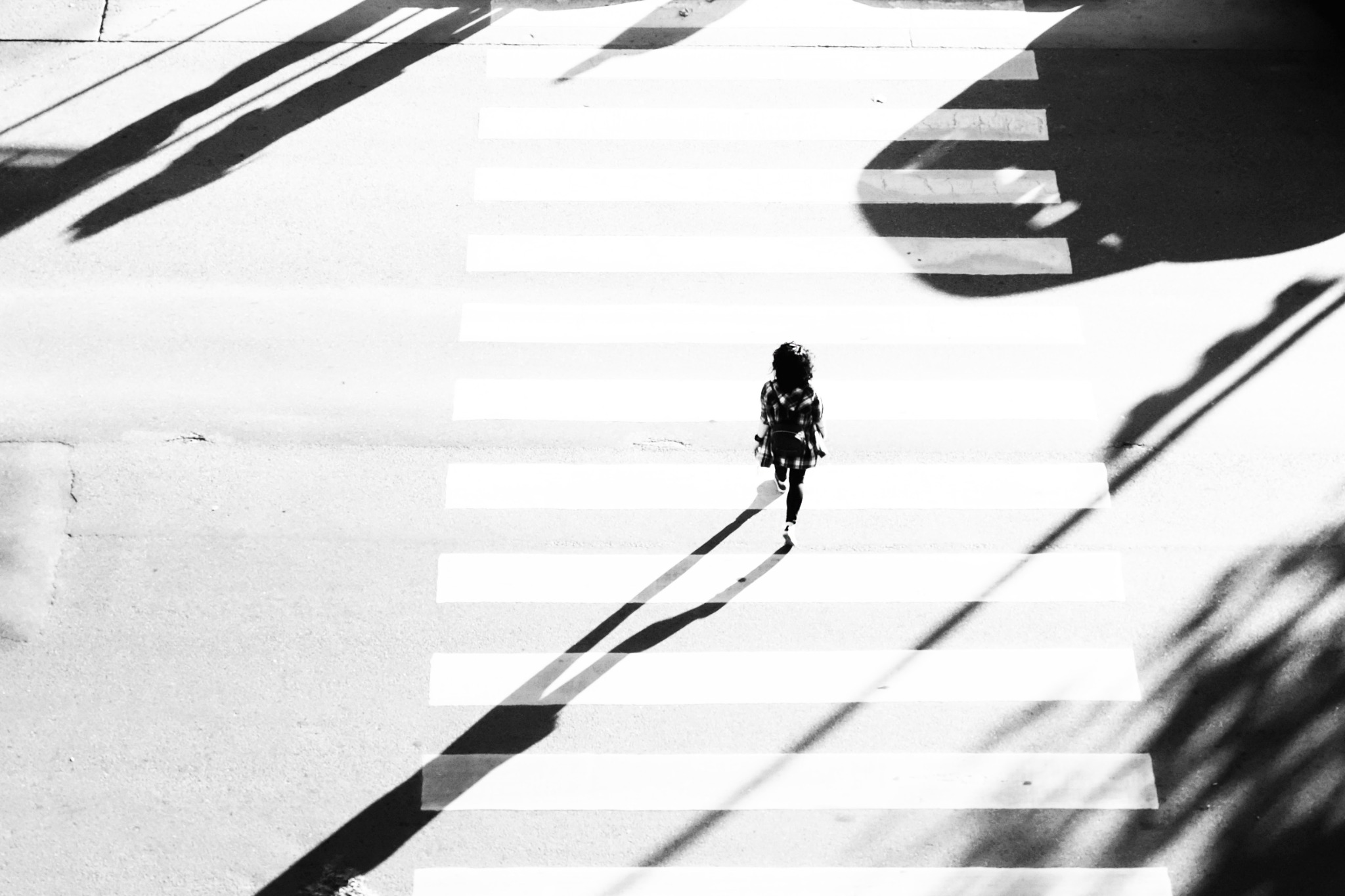 A pedestrian crosses broad white stripes among long diagonal shadows in Buenos Aires.