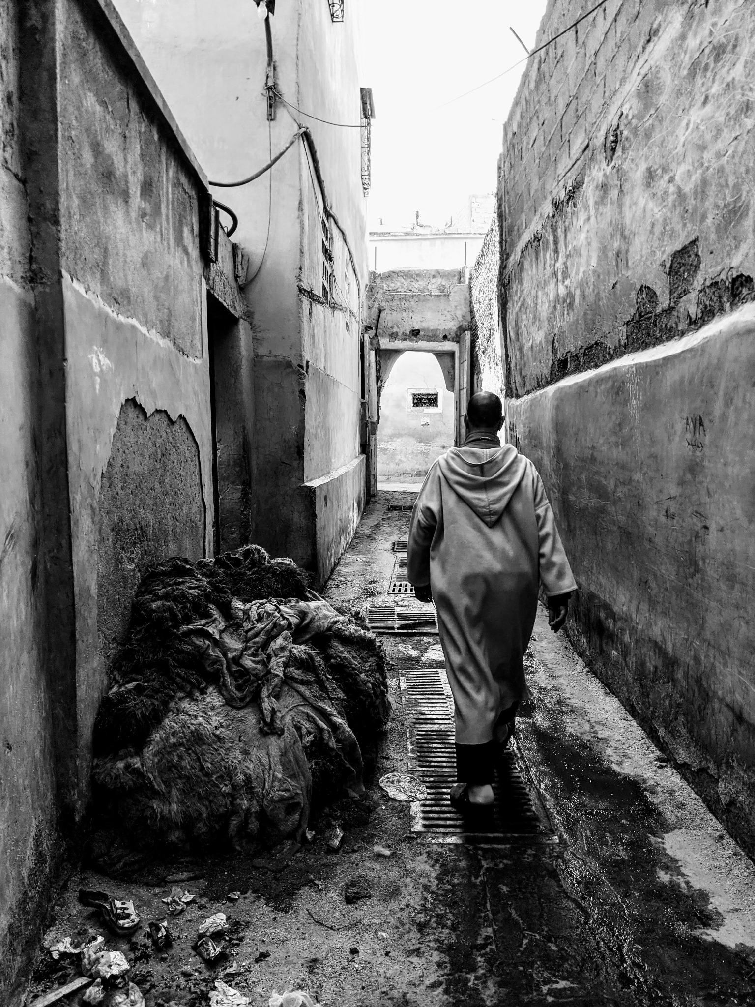 A man walks ahead through a narrow, textured alley in Marrakech, photographed in black and white.