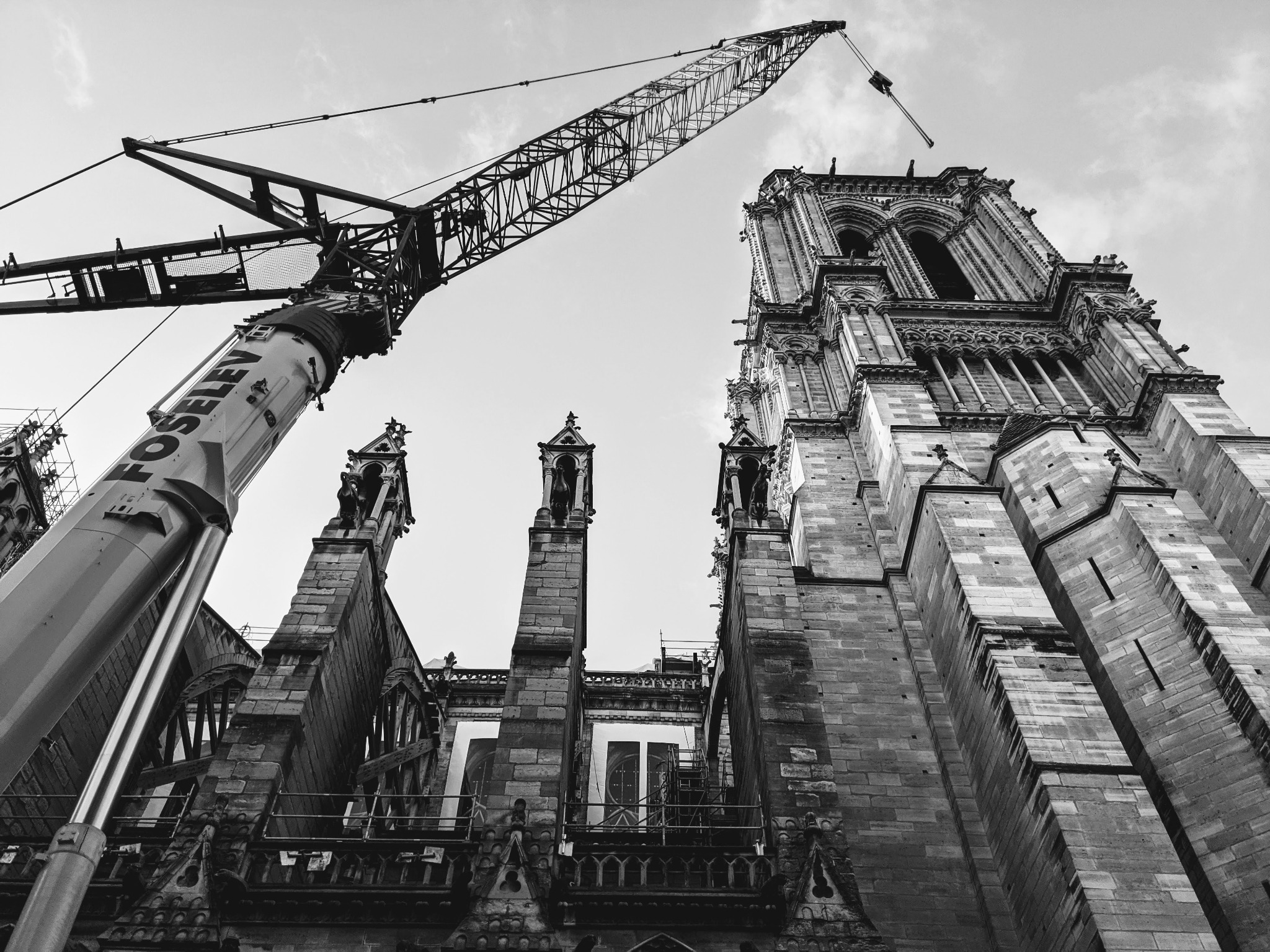 Notre-Dame’s stone architecture and a construction crane cross the sky in a black-and-white photograph.